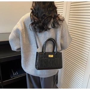 Detail of black crocodile texture bag with gold lock shown on model for realistic scale