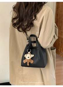 Detail of black pebbled leather bucket bag with monkey charm worn on a khaki trench coat