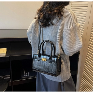 Detail of black crocodile texture handbag with gold hardware shown on person back view