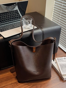 Retro dark brown bucket bag with embossed lettering and metal lock on an office desk