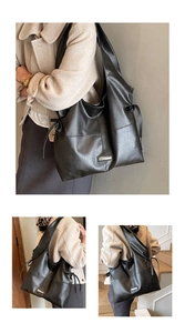 Detailed close-up of large black vintage tote bag with side drawstring and metal label