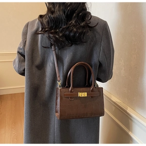 Detail of dark brown crocodile texture shoulder bag with golden metal twist lock and strap