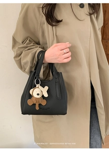 Detail of black lychee grain leather bucket bag with monkey charm held by model