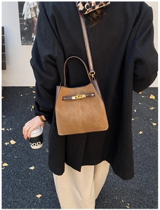 Detail of suede bucket bag with gold hardware and contrast leather trim shown with model