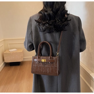 Detail of crocodile embossed leather handbag with gold metal clasp and dual handles