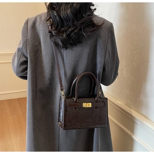 Detail of dark brown faux crocodile leather bag with gold buckle and textured finish