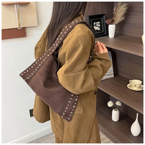 Close-up of brown suede shoulder bag featuring retro gold rivets and metallic eyelets