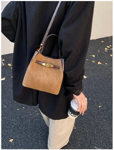 Detailed view of brown suede bucket bag with leather handles and gold metal clasp