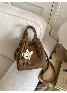 Brown litchi grain leather bucket bag with bear charm on a soft cream sofa