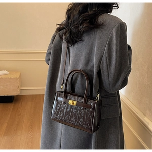 Detail of dark brown crocodile pattern bag with gold clasp and elegant crossbody strap