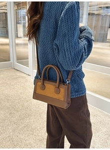 Detail of a brown leather and suede baguette bag shown with a modern textured blue coat
