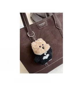 Gros plan d'une peluche de chien avec pull noir sur un sac fourre-tout en cuir marron
