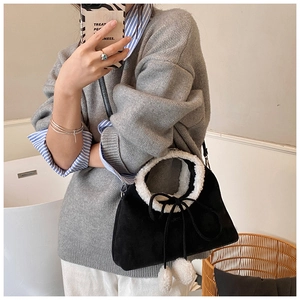 Detail of black suede bag featuring plush white faux fur trim and pom-pom charms