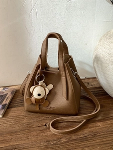 Vintage brown leather bucket handbag with monkey charm on a rustic wooden table