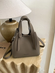 Brown leather bucket bag with top handles and shoulder strap in warm interior setting