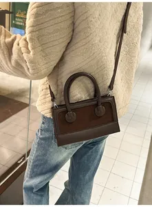 Detail of a dark brown rectangular leather crossbody bag with dual handles on a model