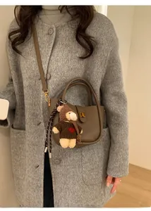 Détail d'un sac cabas en cuir marron avec charm ours en peluche sur un manteau