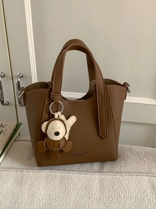 Brown leather bucket bag with top handle and monkey charm in a minimalist interior