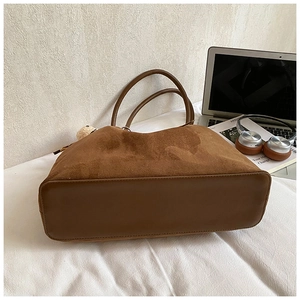 Detailoverzicht van bruine suède tote bag met pluchen beer op witte ondergrond
