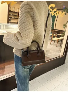 Outdoor shot of a vintage dark brown leather crossbody bag styled with a beige coat
