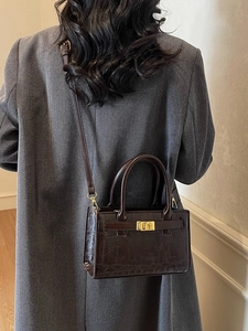 Minimalist dark brown crocodile pattern crossbody bag with gold buckle on a model coat