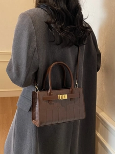 Brown crocodile pattern crossbody bag with gold buckle shown on woman in interior
