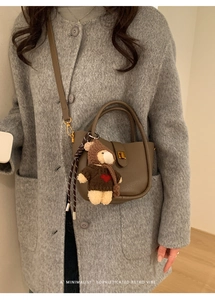 Détail du sac seau en cuir marron avec breloque ours en peluche sur manteau en laine
