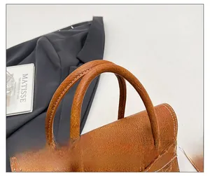 Close-up of brown faux leather handbag showing round handle and white stitching details