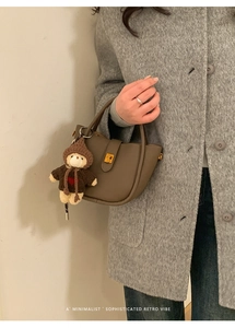 Detail of a brown lychee leather bucket bag with a cute bear charm and golden buckle