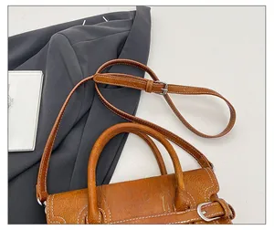 Close-up of brown litchi texture leather handbag with white stitching and silver hardware