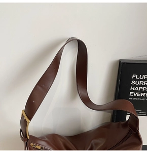 Close-up of a dark brown leather tote bag with wide strap and golden metal buckle details