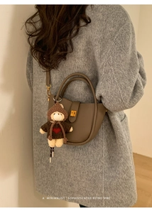 Detail of tan half-moon leather bucket bag with gold clasp and teddy bear charm accessory