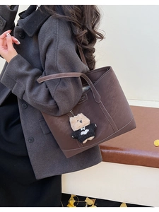 Détail d'un sac cabas en cuir marron avec surpiqûres blanches et pendentif ours mignon