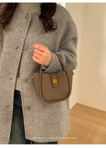 Detail of khaki pebbled leather bucket bag with gold clasp shown on a grey wool coat