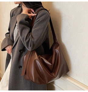 Deep brown leather tote bag with wide strap styled on a grey wool coat against a wall