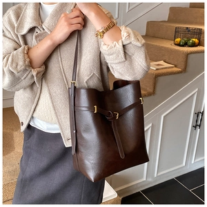 Detailed view of large dark brown leather bucket bag worn over a model's shoulder