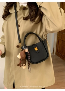 Sac seau rétro en cuir noir avec fermoir doré et charme d'ours sur un manteau beige
