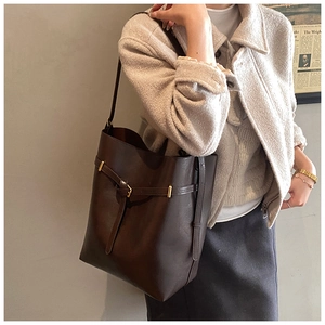 Detail of dark brown bucket tote bag featuring a decorative strap and matte gold buckle