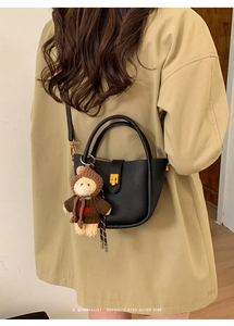 Close-up of black pebble leather tote bag featuring a gold lock and a cute bear charm