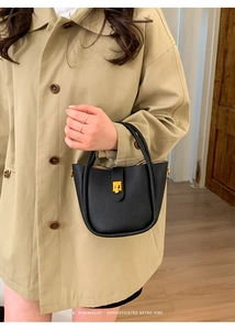 Detail of minimalist black pebbled leather bucket bag with a golden twist lock closure