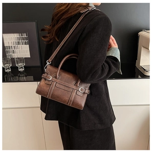 Detail of dark brown leather crossbody bag featuring contrast stitching and silver buckle