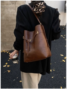 Close-up of brown bucket bag showing decorative buckles and golden hardware details