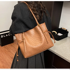 Brown ostrich textured tote bag shown on shoulder with side drawstring and gold buckles