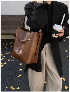 Close-up of brown faux leather bucket bag with gold hardware buckle and rich texture