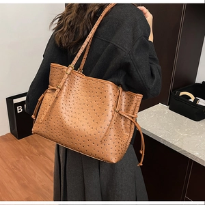Detailed view of brown ostrich-textured tote bag showing PU leather grain and side drawstring