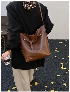 Close-up of a brown leather tote bag with buckle detail shown on model's shoulder