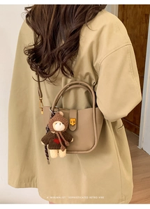 Detail of khaki lychee grain leather bucket bag with gold lock and teddy bear charm