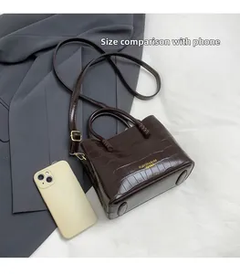 Détail d'un sac seau marron foncé motif crocodile comparé à un smartphone