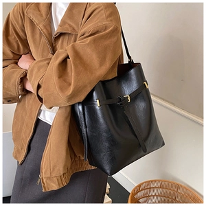 Minimalist black leather tote bag with gold buckle detail worn by a model in casual style