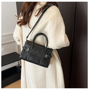 Detail of a black pebbled leather crossbody bag featuring contrasting white stitching and strap